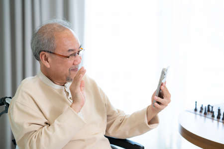 Old man use smart phone and video call to his family with smile but alone from nursing homeの写真素材