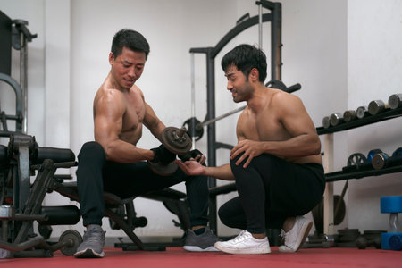 Asian man trains in the gym. Athletic man trains with dumbbells, pumping his bicepsの写真素材
