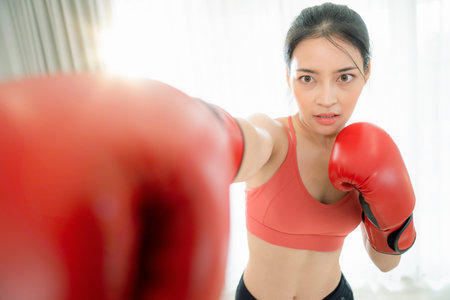Asian woman exercise and boxing in her bed room, her try to make slim by take Yoga, cardio, fitness at home between quarantineの写真素材