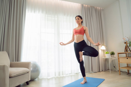 Asian woman exercise and stretching in her bed room, her try to make slim by take Yoga, cardio, fitness at home between quarantineの写真素材