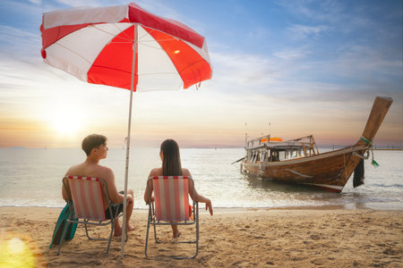 Asian traveller couple sitting and see sunset togather on the beach with longtail boat background at Phi phi island maya beach near Phuket, Thailandの写真素材