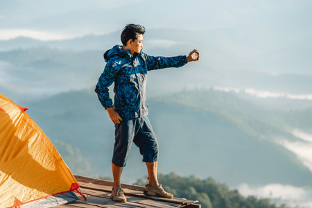 Asian traveller man take a photo by her camera on the top of mon Kalakojo at Tak with sunrise and fog background on the morning time, Winter season of view point near Chiang mai, Thailandの写真素材