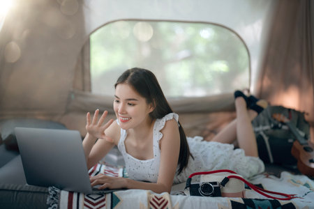 Asian woman traveller sleep and relax with her computer note book use internet for greeting with her family on ther bed in her tent in her camping tripの写真素材