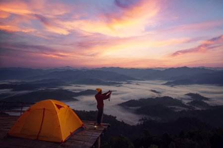 Asian traveller woman take a photo by her camera on the top of mon Kalakojo at Tak with sunrise and fog background on the morning time, Winter season of view point near Chiang mai, Thailandの写真素材