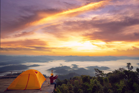 Asian traveller woman take a photo by her camera on the top of mon Kalakojo at Tak with sunrise and fog background on the morning time, Winter season of view point near Chiang mai, Thailandの写真素材