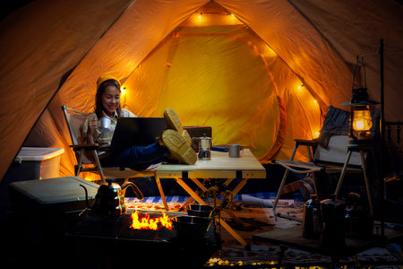 Asian woman enjoy in they tent in camping trip on night time with many star on the sky, they enjoy coffee, working by coputer notebook and not book and relax in campの写真素材