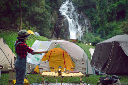 Asian traveller woman plan her trip by a map at ter tent in camping with waterfall background, at Chiang mai, Thailandの写真素材