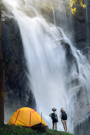 woman traveller walk togather Tent and camping with Mae Tia waterfall and mountain background at inthanon national park in Chiang mai, Thailand, un seen travel point for camping and relax in holidayの写真素材
