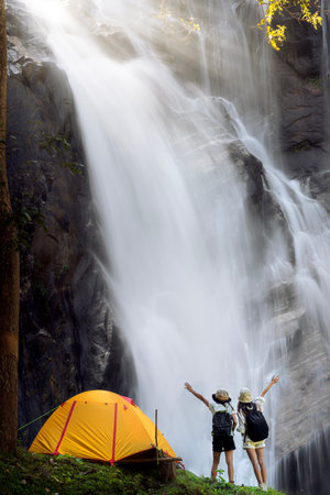 woman traveller walk togather Tent and camping with Mae Tia waterfall and mountain background at inthanon national park in Chiang mai, Thailand, un seen travel point for camping and relax in holidayの写真素材