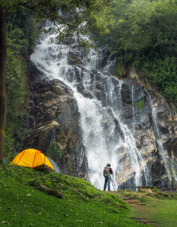 A man traveller walk togather Tent and camping with Mae Tia waterfall and mountain background at inthanon national park in Chiang mai, Thailand, un seen travel point for camping and relax in holidayの写真素材