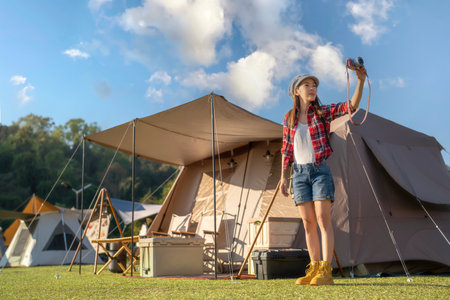 Asian traveller woman middle age take a photo by her digital camera at her tent in camping location at chiang mai, Thailandの写真素材