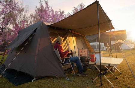 Asian couple enjoy in they tent in camping trip on night time with table, cup, mug and party inside tent, they enjoy coffee, working by coputer notebook and not book and sweet in campの写真素材