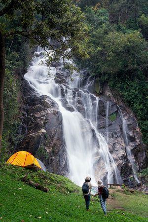 woman traveller walk togather Tent and camping with Mae Tia waterfall and mountain background at inthanon national park in Chiang mai, Thailand, un seen travel point for camping and relax in holidayの写真素材