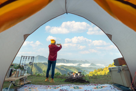 Woman traveller take a photo by her smartphone for keep a mountain view in front of her tent in campingの写真素材