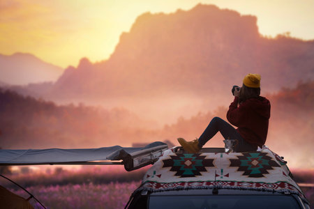 Traveller woman sit on the roof top tarp and car and drink a coffee with morning sunrise and fog on the mountain view, Chiangmai, Thailandの写真素材