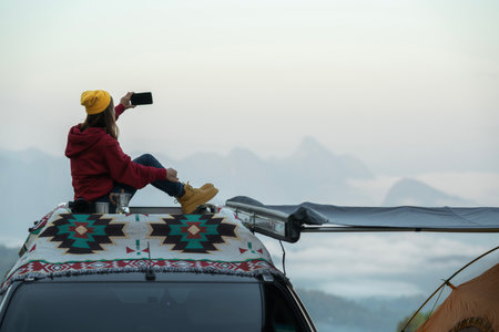 Traveller woman sit on the roof top tarp and car and drink a coffee with morning sunrise and fog on the mountain view, Chiangmai, Thailandの写真素材