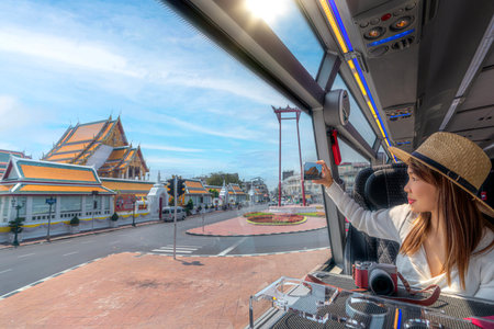 Asian traveller woman take a photo the giant swing and wat suthat on the restaurant bus between city tour by bus in Bangkok, Thailandの写真素材