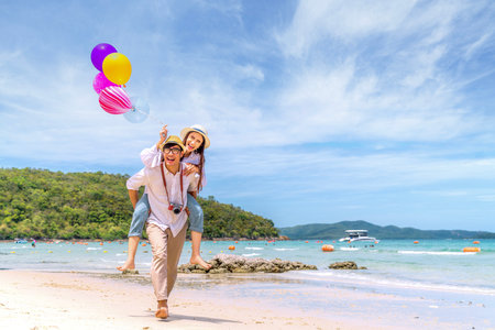 Asian couple travel Thailand beach todather, run and take a balloon on the beach in summer time between they holidayの写真素材
