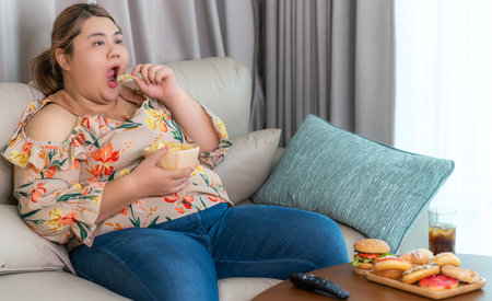 Asian over size fat woman enjoy over eating on the living room, un healthy foods and junk food concept photoの写真素材