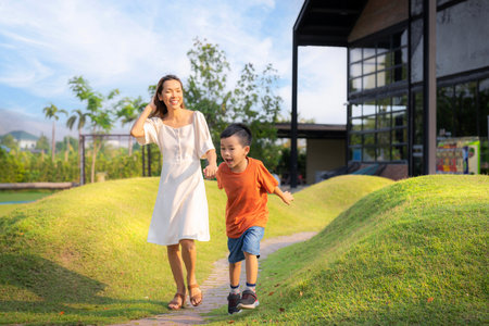 Asian mother and her som running togather on the garden with green grassの写真素材