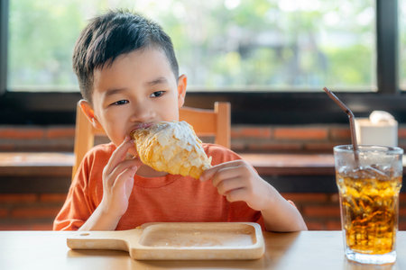 Asian boy eating  sweet croissant in restaurant with beverage on the tableの写真素材