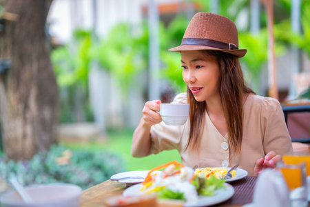 Asian traveller woman eating buffet breakfast in hotel restaurant on outdoor zone area with cofee and saladの写真素材