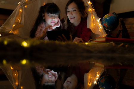 Asian Mother and daughter relax with tent and light in they bed room and read a teblet togather on night time at homeの写真素材