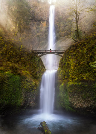 Multnomah Falls view with sunrise and traveller woman standing on the bridge, columbia river gorge,...