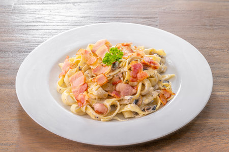 mushroom cream sauce spaghetti with bacon on white dish put on the wooded table in italian restaurantの写真素材