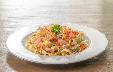 mushroom cream sauce spaghetti with bacon on white dish put on the wooded table in italian restaurantの写真素材