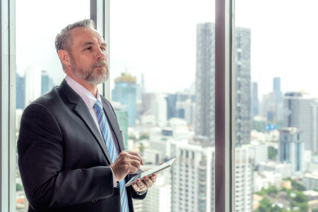Old man manager use tablet in his office working in rooftop meeting room, Bangkok, Thailandの写真素材