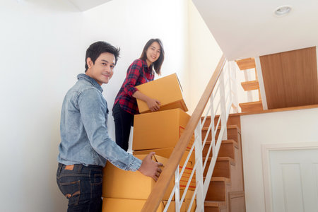 Asian couple just new married husband and his wife carry a paper box togather on stairs for move it to home second floor for move in to new house and start fot new sweet familyの写真素材