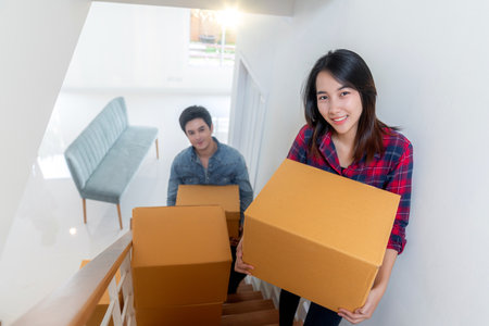 Asian couple just new married husband and his wife carry a paper box togather on stairs for move it to home second floor for move in to new house and start fot new sweet familyの写真素材