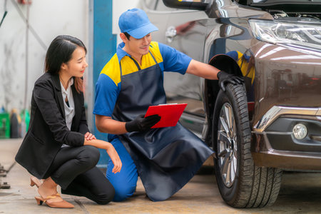 repairman and technician in car garage service in blue uniform standup and smile with tooling on hand for car check with car ownerの写真素材