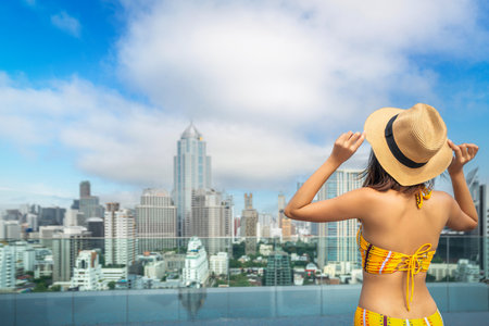 Asian traveller woman sleep and relax at swimming pool on hotel roof top with Bangkok city view, Thailandの写真素材