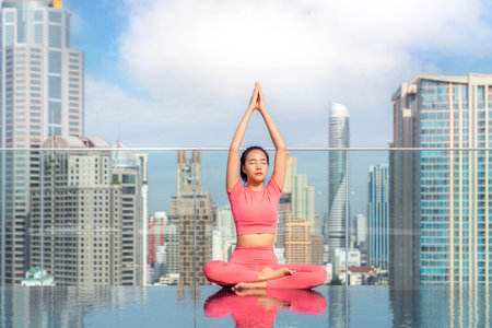 Asian woman pose yoga action on hotel rooftop with Bangkok city and swimming pool background, basic pose for Pilate actionの写真素材