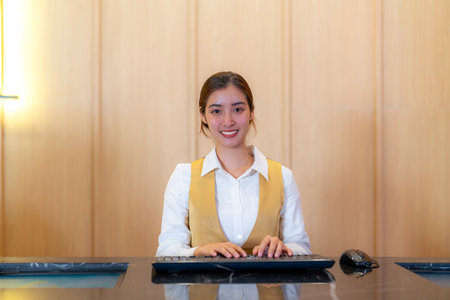 Smile asian ticket clerk in front of cinema theater sales a ticket for a movie on the counter, woman receptionist in hotel reception desk with monitor buil in the deskの写真素材