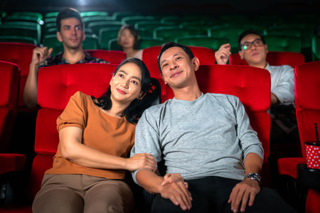 Happy trip of asian couple sweet sit togather on red seat and looking  movie in cinema with fun a popcorn on hand, people relax and holiday activity on a weekendの写真素材