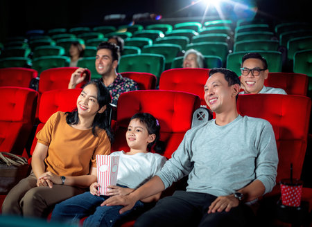 Happy trip of asian family sit togather on red seat and looking  movie in cinema with fun a popcorn on hand, people relax and holiday activity on a weekendの写真素材