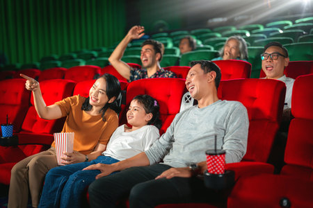 Happy trip of asian family sit togather on red seat and looking  movie in cinema with fun a popcorn on hand, people relax and holiday activity on a weekendの写真素材