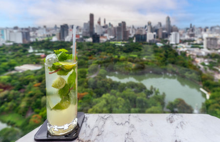 glass of mojito on the roof top bar table with Bangkok city vier and park in Thailandの写真素材