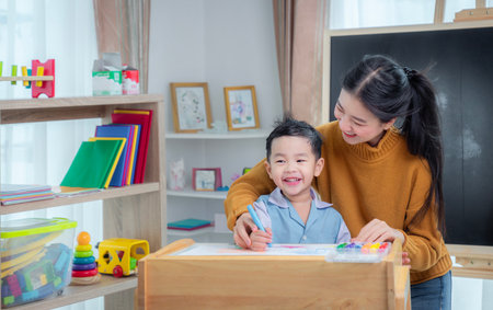 Asian teacher and her kindergarten student draw and paint art work together in class room in schoolの写真素材