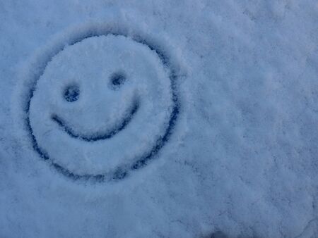 Snow and ice and a smiley on a frozen window glass against a blue skyの写真素材