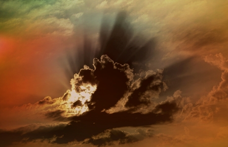 Sunbeams shine through gloomy clouds and color the sky in dark, breathtaking colorsの写真素材