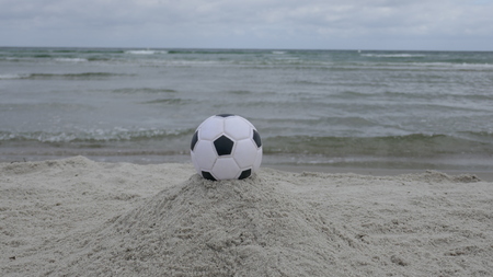 A black-and-white soccer ball reads at the beach in the background, close-upの写真素材