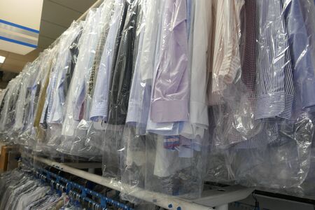 Freshly cleaned men's shirts and ladies blouses in textile cleaning, hung on hangers and protected by plastic film. Ready for pick upの写真素材