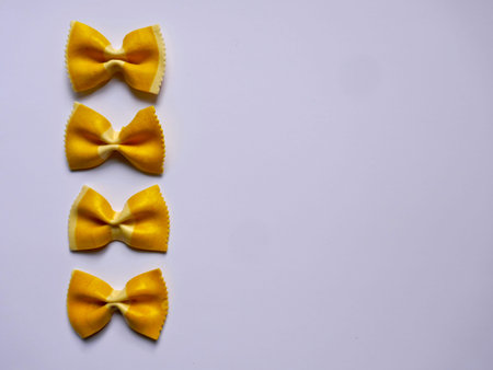 Colorful Pasta, Loop Noodles, Italian Pasta. Four yellow farfalle in a row, one below the other, in...