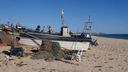 Armacao de Pera, Algarve, Portugal - March 4, 2019: Fishermen mending their nets. At the long, wide, fine sandy fisherman beachのeditorial素材