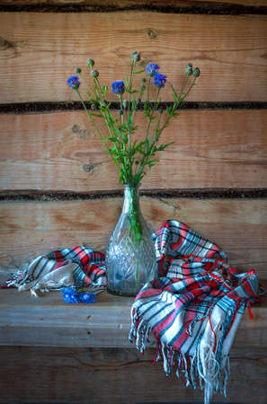 Beautiful still life with blue flowers in a glass vase and a beautiful shawl in the old rural wooden houseの写真素材