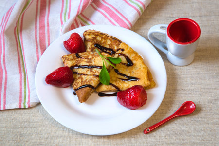 Beautiful baked pancakes with red berries and chocolate on a white plate. On the table linen towel...